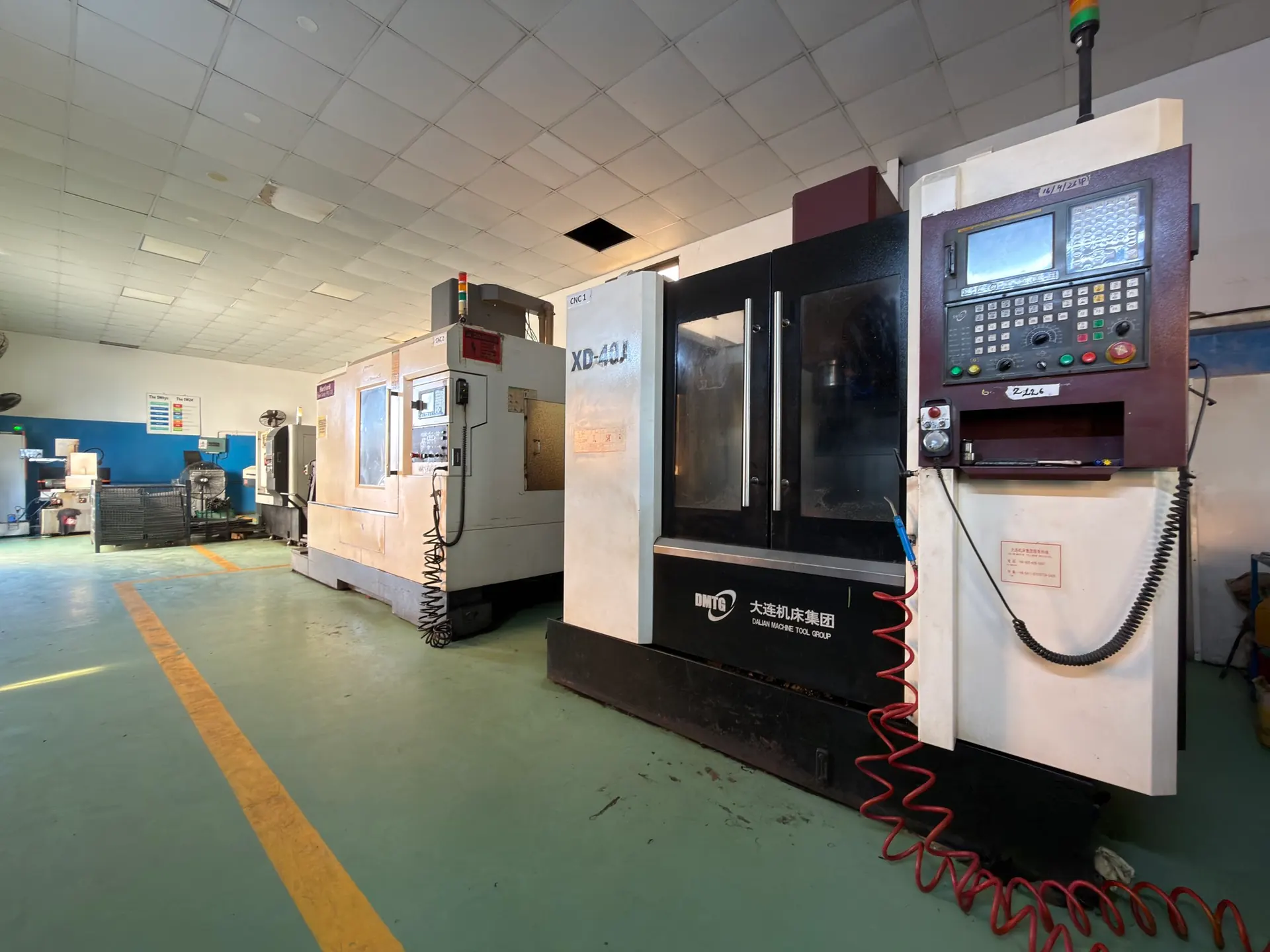 Row of CNC vertical machining centres on a green epoxy floor, with a DMTG XD-40A in front