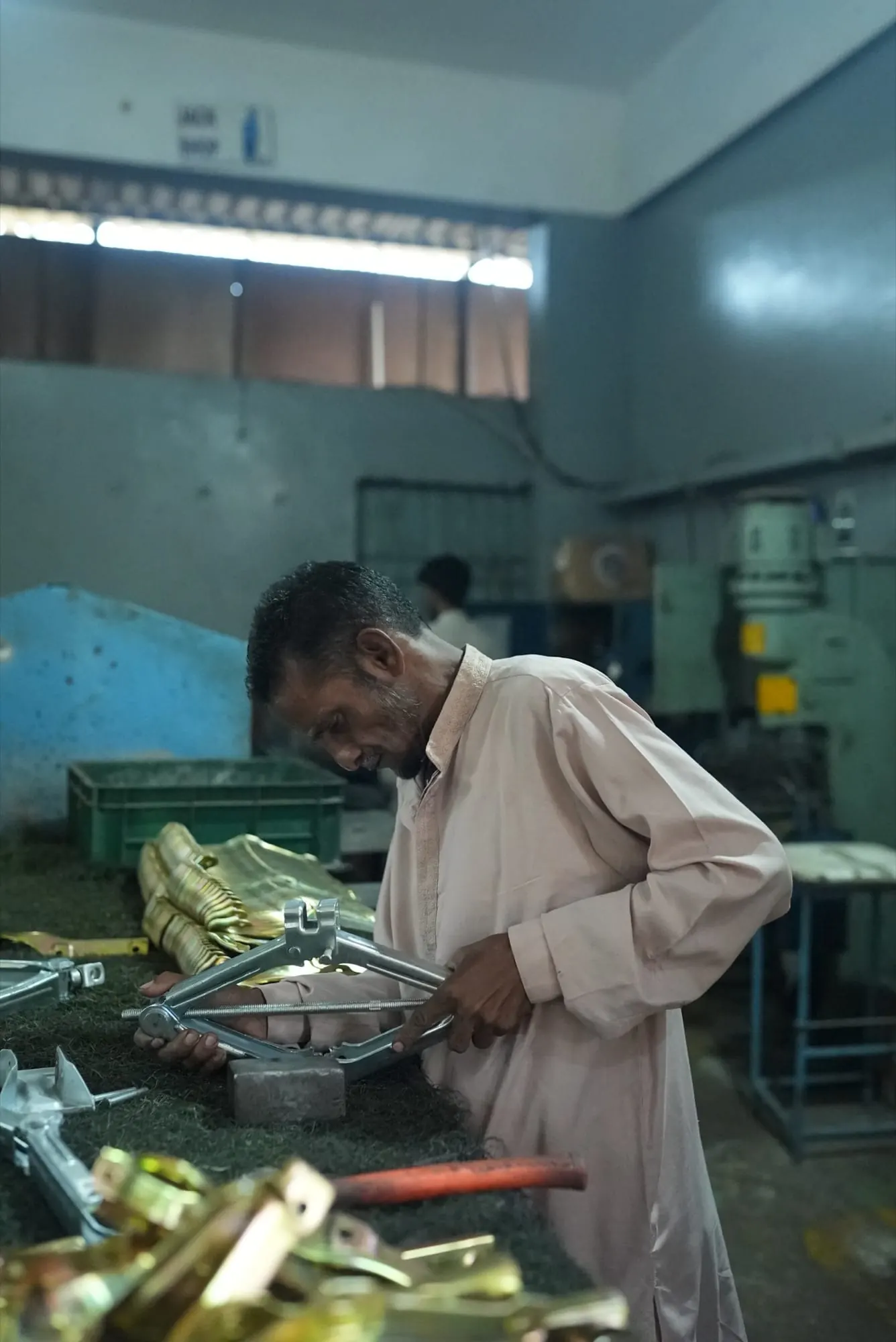 Worker assembling a zinc-plated scissor jack at a bench stacked with jack components