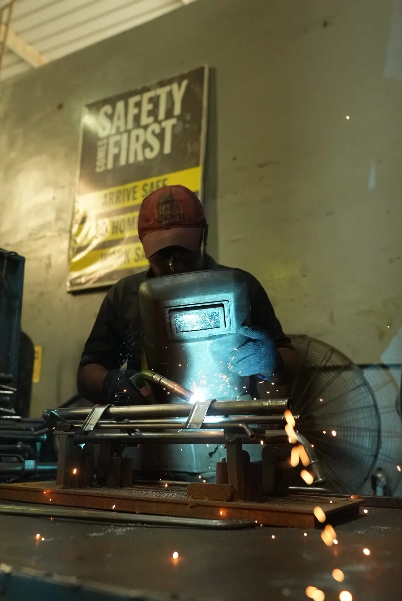 Welder holding a hand shield while welding a pipe assembly on a fixture