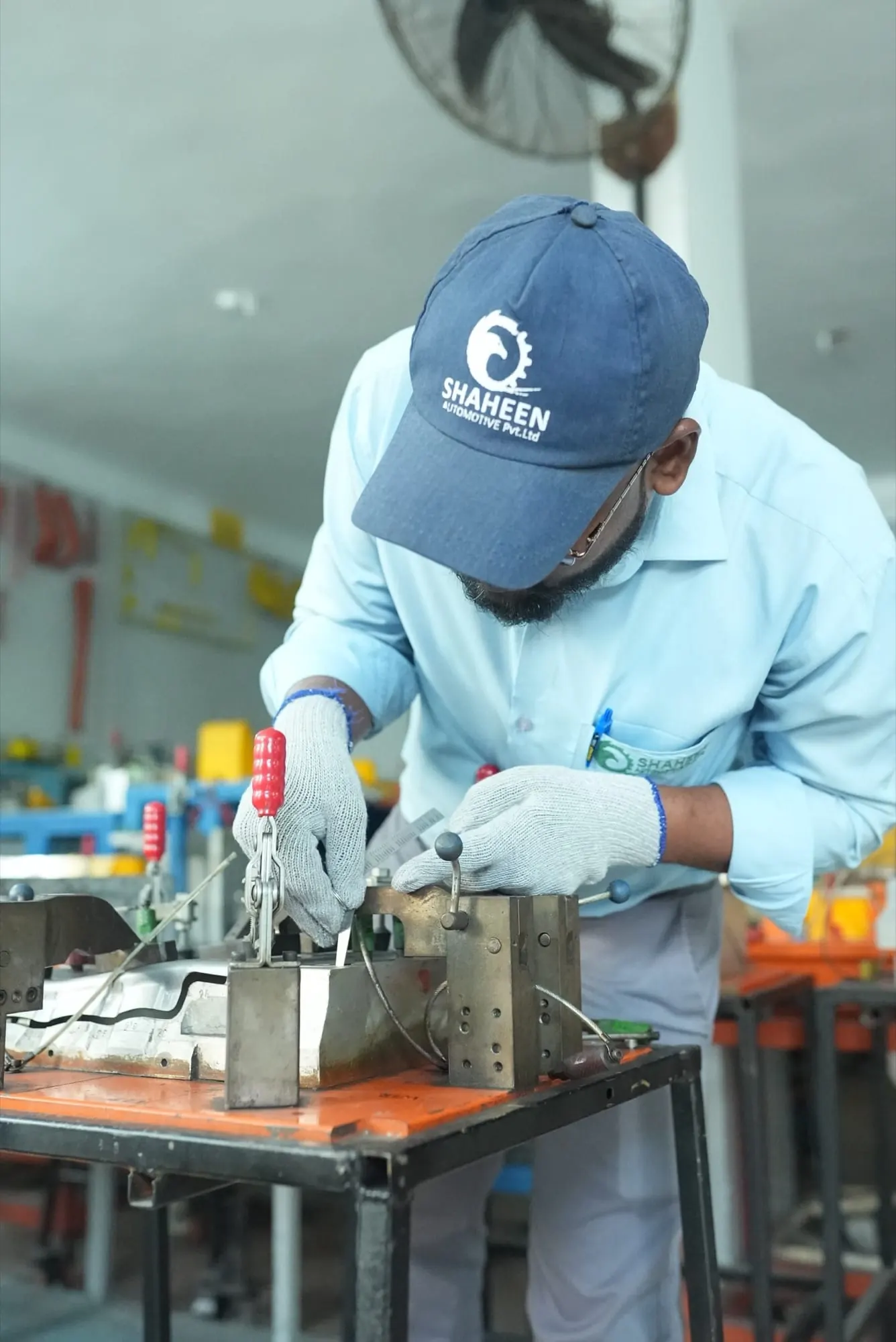 Inspector in a Shaheen Automotive cap checking a clamped panel with a gauge