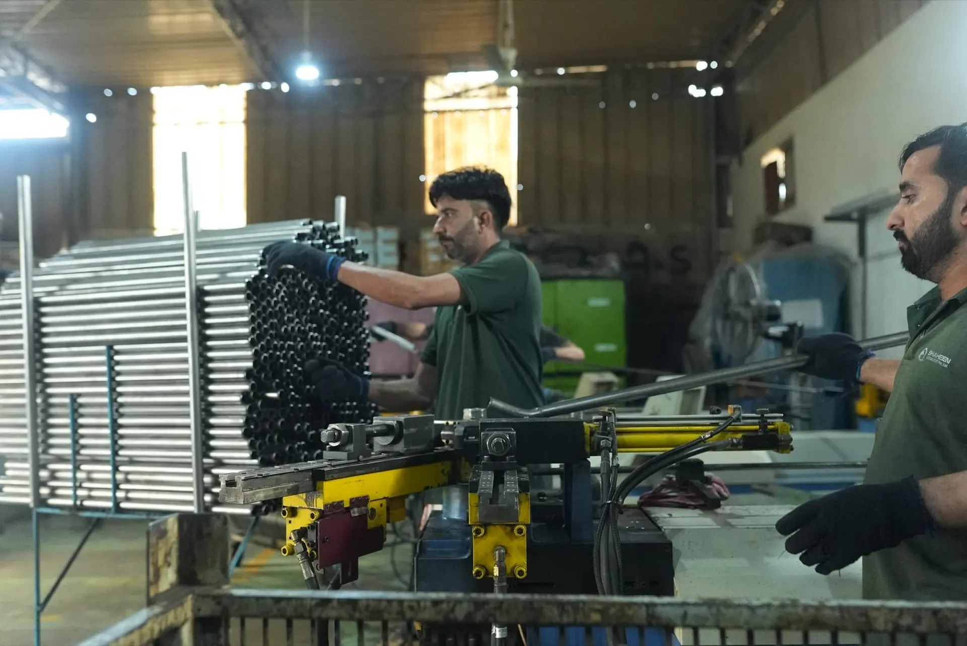 One operator unloading a bent tube while another pulls stock from a stack of steel tubes