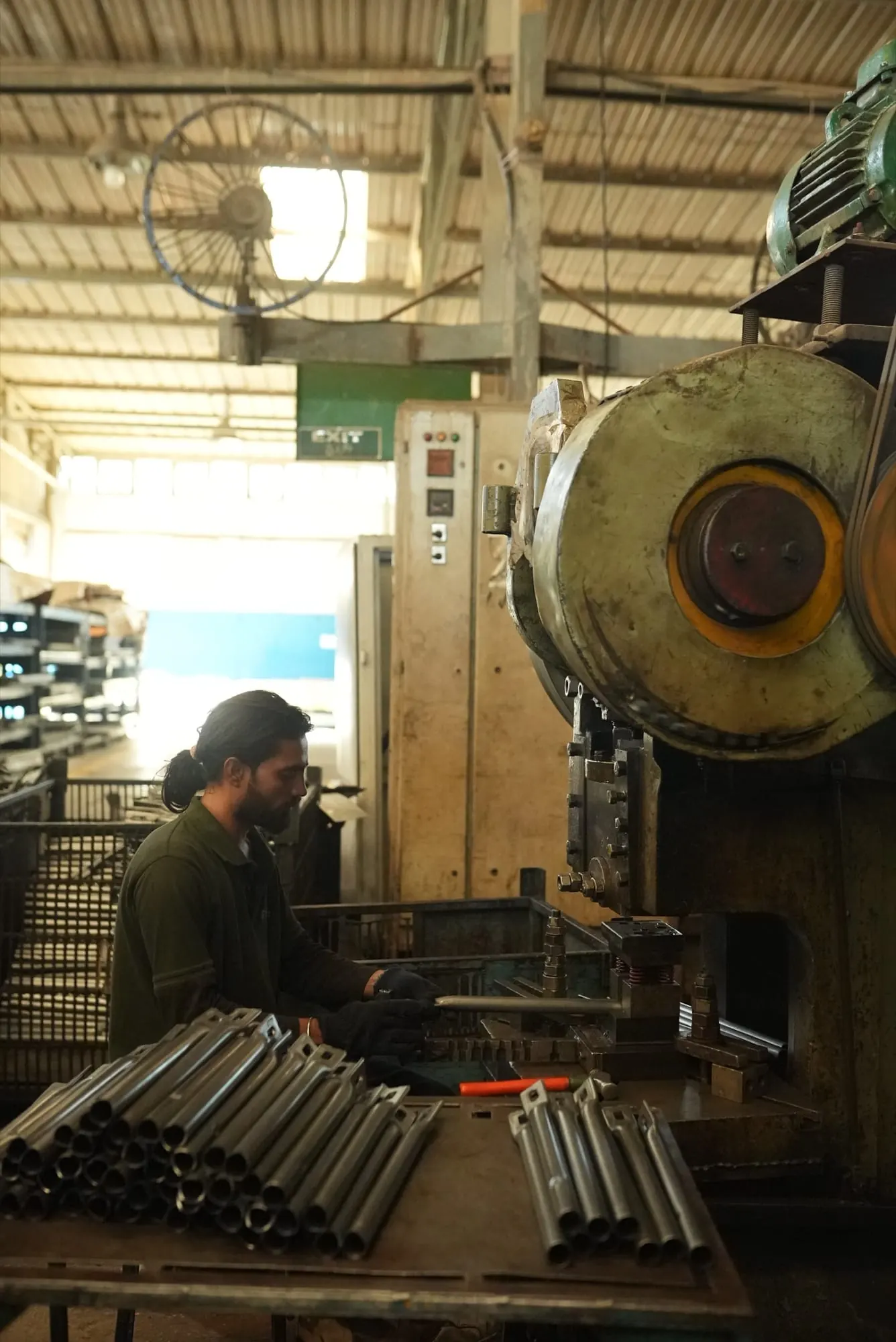 Operator forming the ends of steel tubes on a power press, with finished tubes stacked on the table
