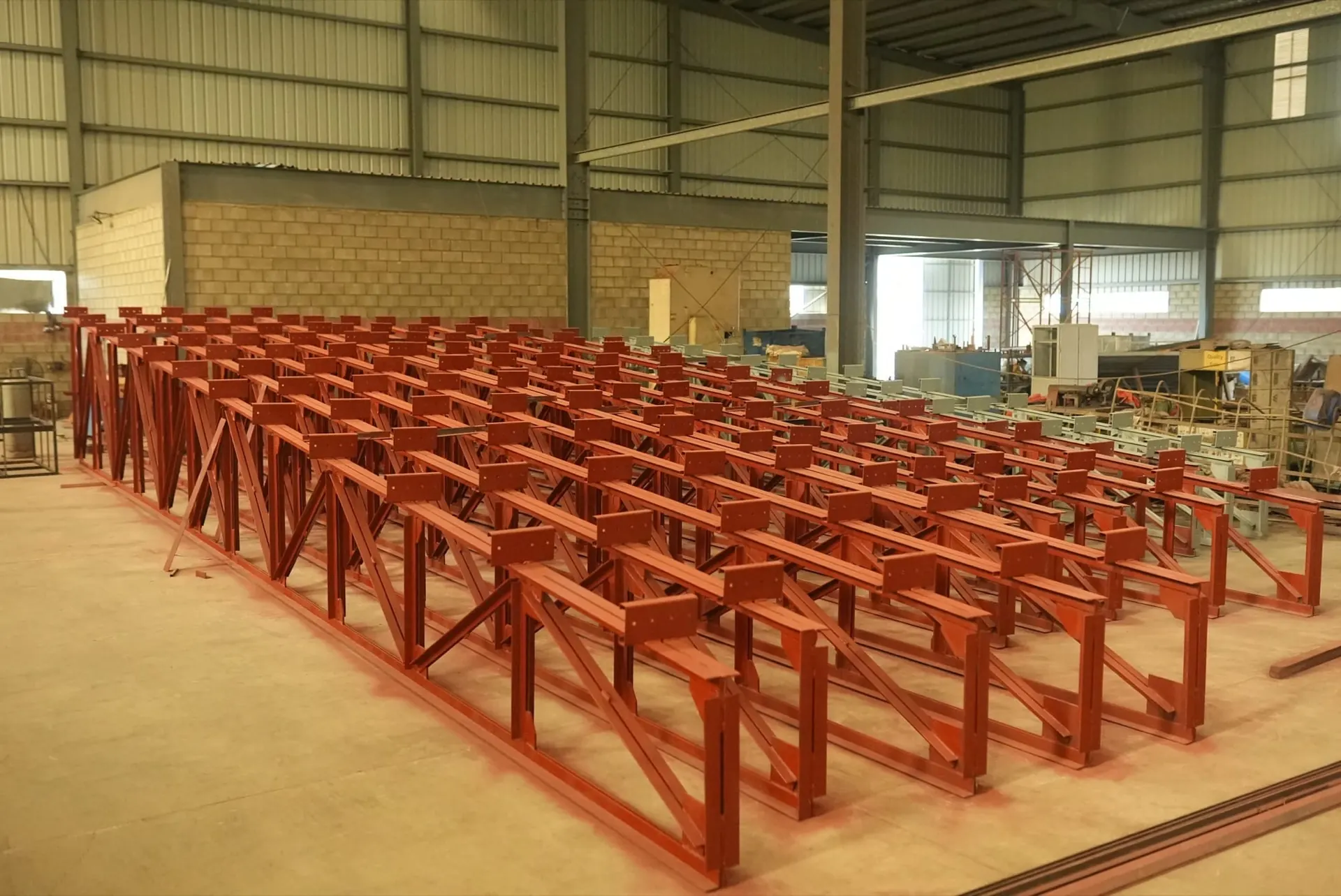 Rows of welded steel frames finished in red primer on the shop floor