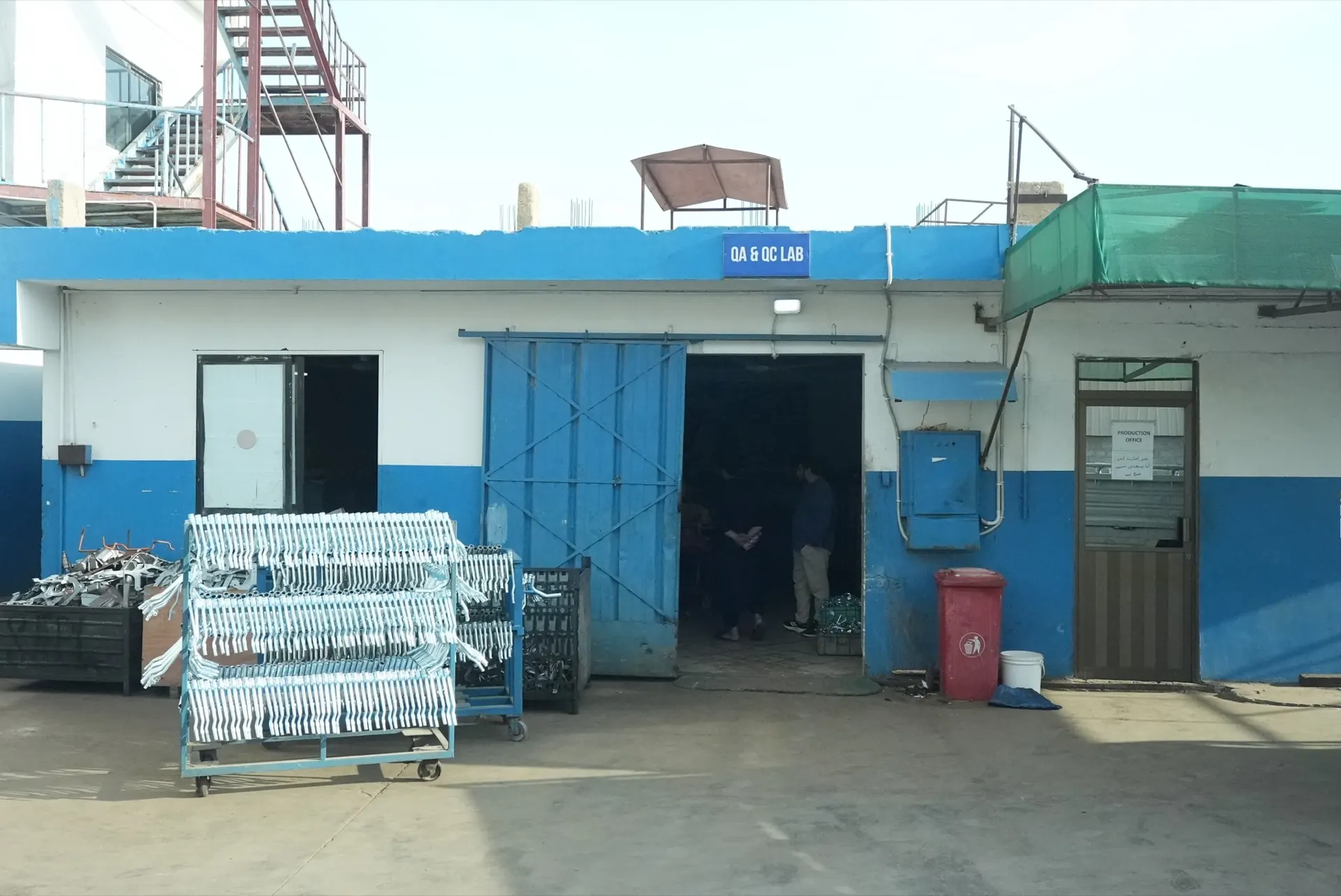 Entrance to the QA & QC lab beside the production office, with racks of finished parts outside