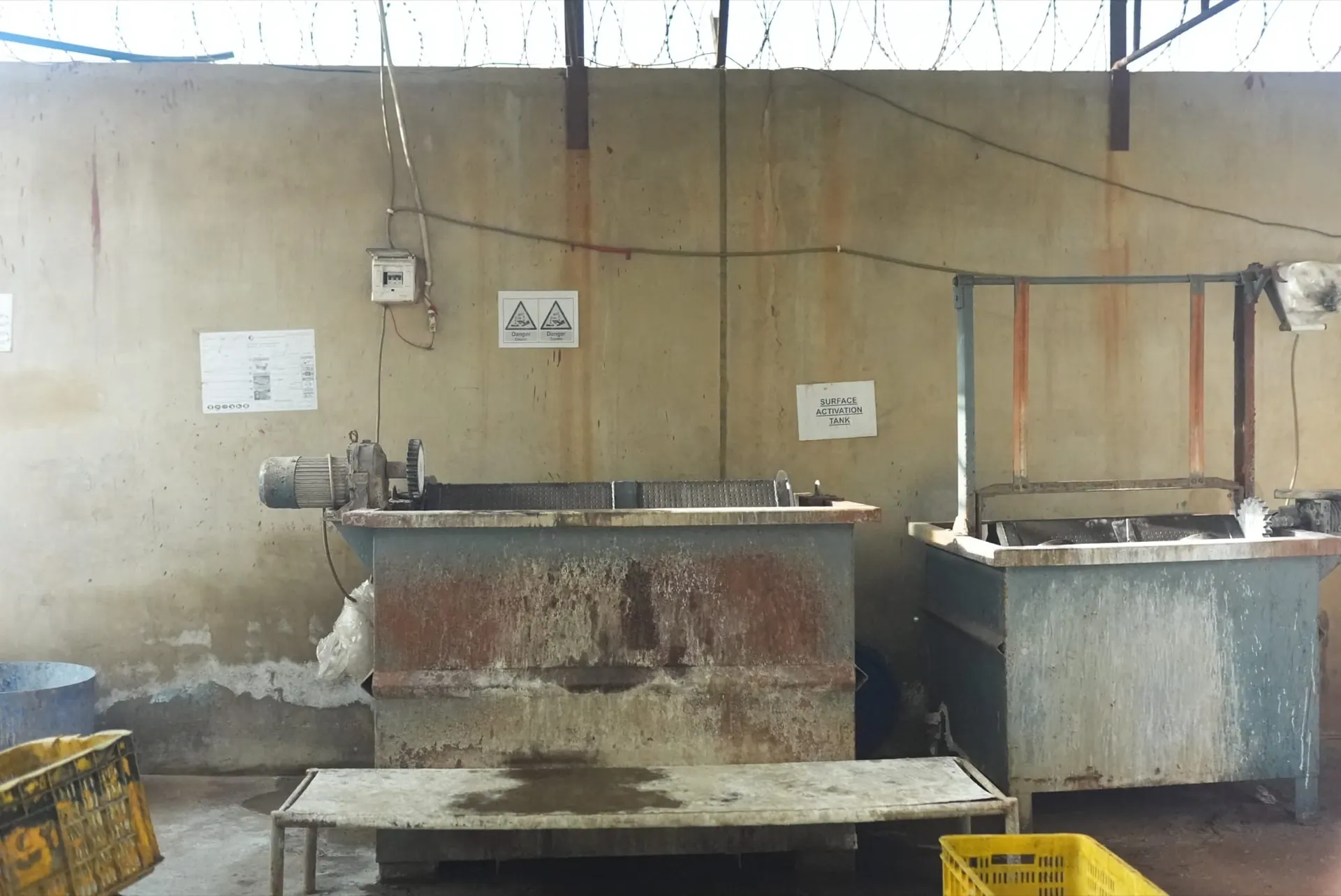 Two barrel tanks against the wall under caustic hazard and surface activation signs